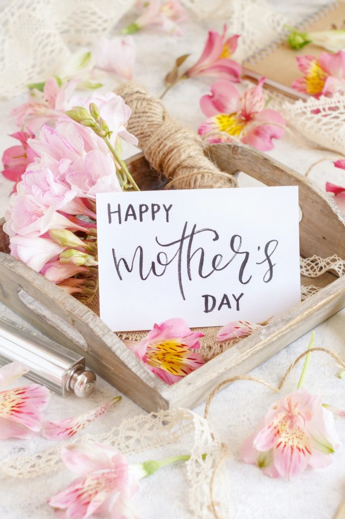 Happy Mother's Day handwritten card on a wooden tray between pink flowers
